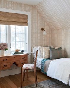 a bed sitting under a window next to a wooden desk and chair in a bedroom