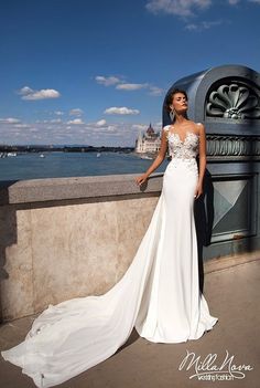 a woman in a white wedding dress standing on a ledge next to the water and looking off into the distance