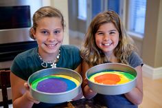 two girls are holding pans with colored food in them