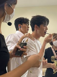 three people with masks on and one holding something in his mouth while the other is wearing a face mask