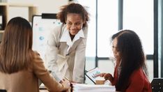 three women sitting at a table in an office talking to each other and one is holding a folder