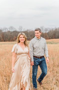 a man and woman standing next to each other in the middle of a field with tall grass