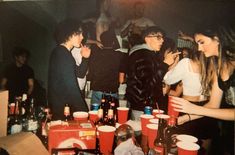 a group of young people standing around a table full of drinks and sodas,