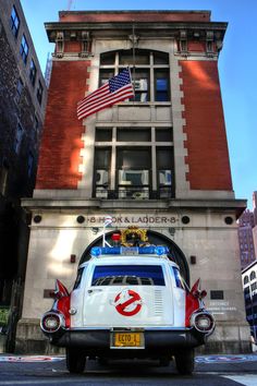 an old ambulance parked in front of a tall building with american flag on it's roof