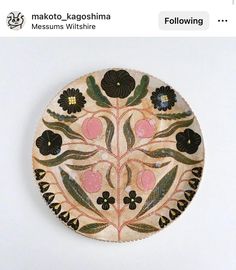 a decorative plate with flowers and leaves painted on the front, sitting on a white surface