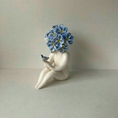 a white ceramic figurine with blue flowers in it's hair sitting on the ground