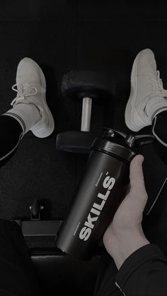 a person holding a black coffee cup next to their feet on a gym equipment floor