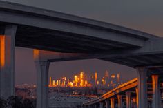 the city lights shine brightly in the distance as seen from under an elevated highway bridge