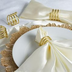 a white plate topped with gold napkins next to some rings and napkin holders on top of a table