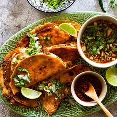 some tacos are on a green plate with salsa and limes next to it