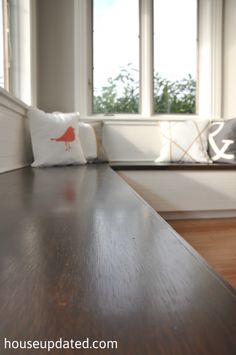 a wooden table in front of a window with two pillows on it and a bench behind it