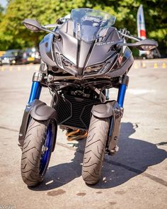 the motorcycle is parked on the pavement in front of some trees and bushes, it's all black with blue accents