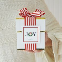 a person holding a small gift box with a ribbon on the top that says joy