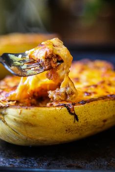 a fork in a baked potato dish with meat and cheese on the top, being lifted from it