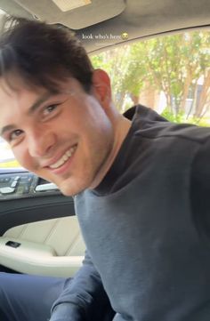 a man sitting in the back seat of a car smiling at the camera with his hand on the steering wheel