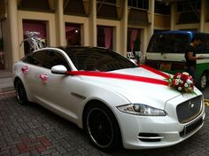 a white car with red ribbon and flowers on the hood is parked in front of a building