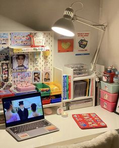 a laptop computer sitting on top of a desk next to a lamp and bookshelf