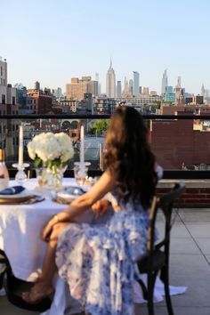 a woman sitting at a table with a view of the city in the back ground