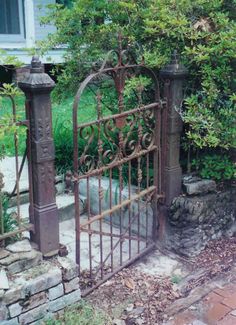 an old iron gate in the middle of a garden with rocks and plants around it