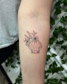 a woman's arm with a flower and seashell tattoo on the left forearm