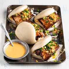 some food is sitting on a metal tray with sauce in a bowl next to it