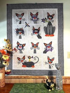 a quilted wall hanging with cats on it's sides and two stuffed animals sitting next to it