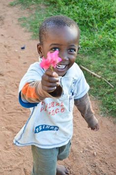 a young boy holding a pink flower in his right hand and pointing at the camera