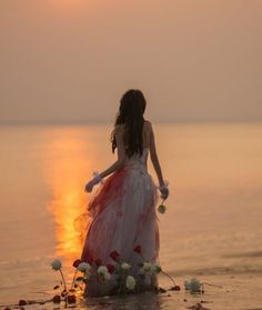 a woman standing in the water at sunset with flowers on her head and hands behind her back