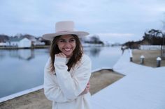 a woman wearing a white hat standing next to a body of water