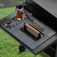 an outdoor bbq grill with two knives and a bottle on the table next to it