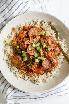 a white bowl filled with rice and meat next to a fork on top of a table