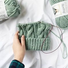 someone is knitting something on the bed with their hands and two balls of yarn next to them