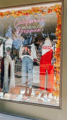 a window display with mannequins and other items in the front, behind which are orange leaves