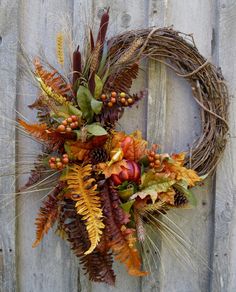 a wreath with autumn leaves and berries hanging on a fence