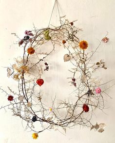 a circular wreath made out of branches and dried flowers on a white wall with strings hanging from it