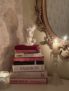 a stack of books sitting on top of a table next to a candle and mirror