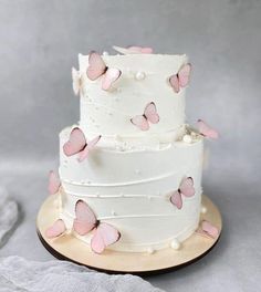 a three tiered cake with pink butterflies on the icing and white frosting