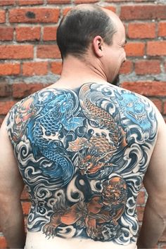 a man with a dragon tattoo on his back is standing in front of a brick wall