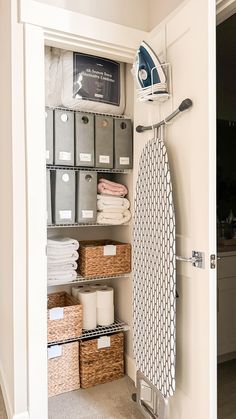 an ironing board is in the closet next to some baskets and boxes with towels