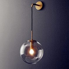 a glass ball light hanging from the side of a gray wall with a gold metal hook