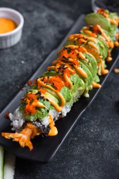 a black plate topped with sushi covered in sauce