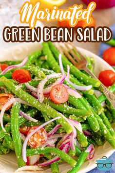 green bean salad with tomatoes and onions on a white plate next to a blue towel