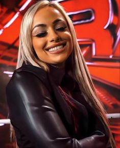 a woman with long blonde hair and black leather jacket smiling at the camera while standing in front of a red background