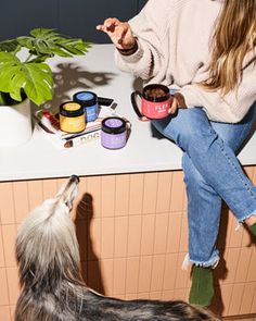 a woman sitting on a counter next to a dog with her paw in the air