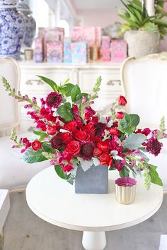 a white table topped with a vase filled with red and pink flowers next to a chair