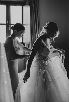 black and white photograph of two women in wedding gowns looking at each other's dresses