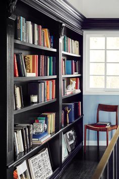 a bookshelf filled with lots of books next to a wooden chair and window