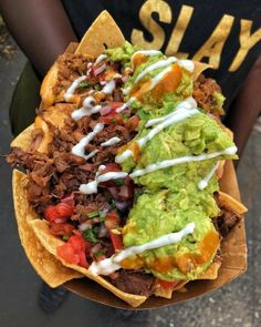 a person holding a paper plate filled with tacos and guacamole