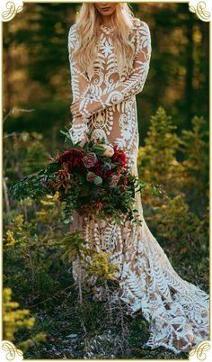 a woman standing in the woods wearing a long sleeved dress and holding a bouquet