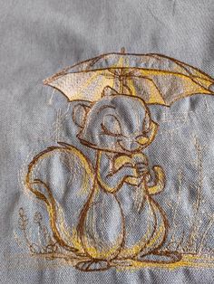 a drawing of a squirrel holding an umbrella on top of a blue shirt with yellow thread